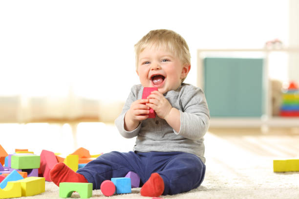 A baby boy is laughing whilst sitting and holding a block