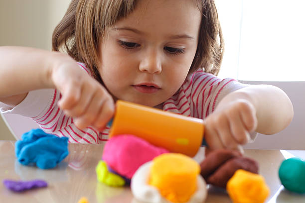 A toddler girl is pictured using a rolling pin to roll out plastercine